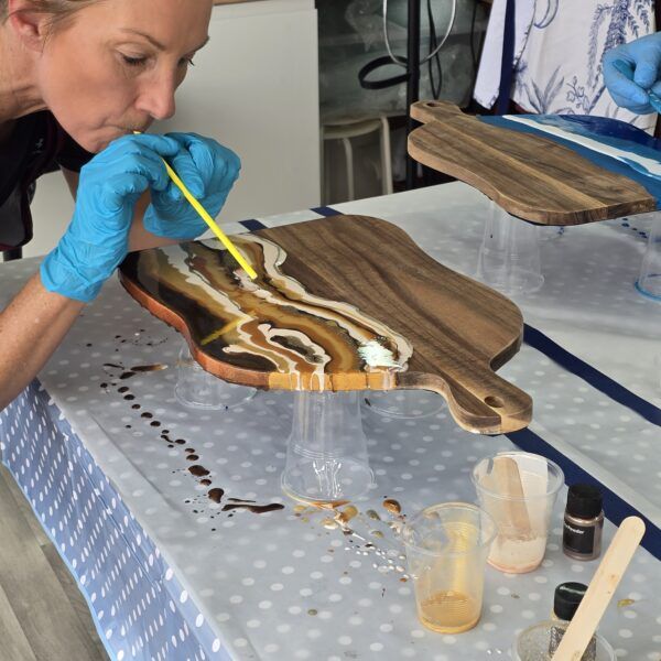 Close up of lady wearing blue protective gloves blowing paint on wooden board.