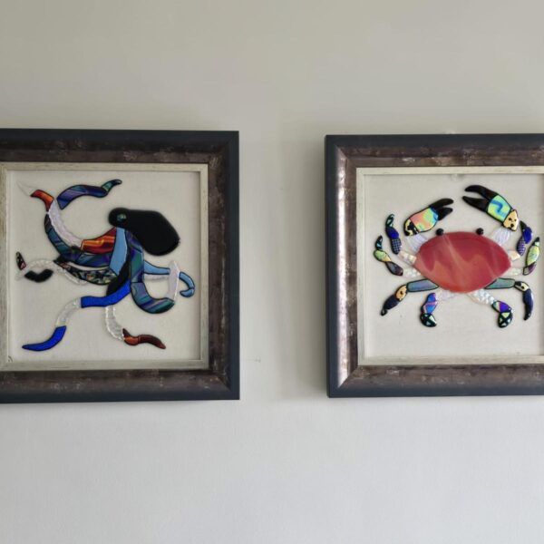 Two framed pictures on a wall depicting an octopus and crab made from glass / resin.