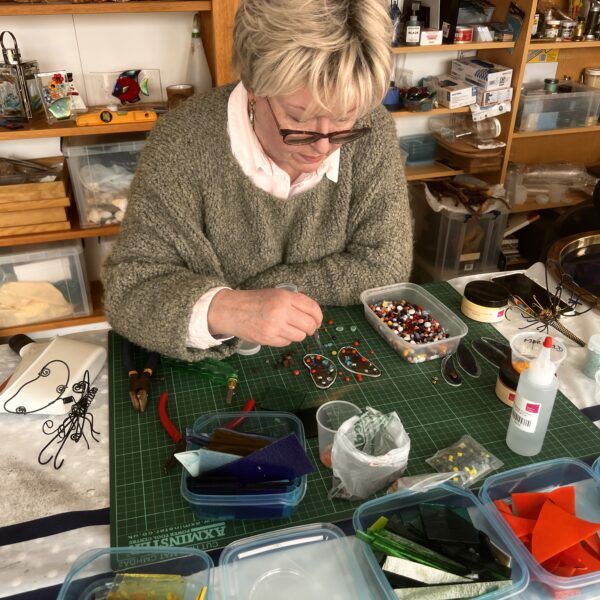 Lady sitting at workshop table working with small pieces of glass.