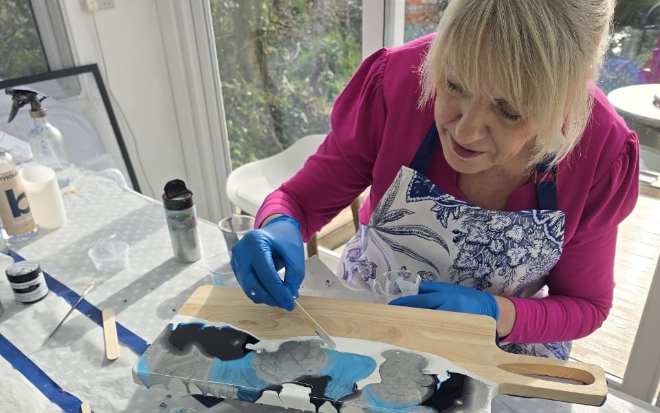 Julia Ford in pink blouse working with paint in front of window.