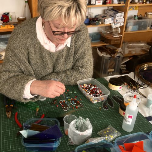 Lady sitting at workshop table picking glass to make mosaic butterfly.