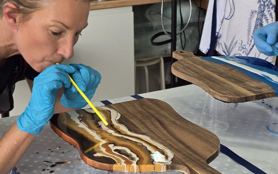 Close up of lady wearing blue protective gloves blowing paint on wooden board.